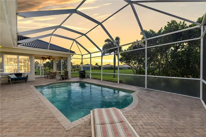Pool at dusk with a sunroom, an outdoor pool, a patio area, and glass enclosure