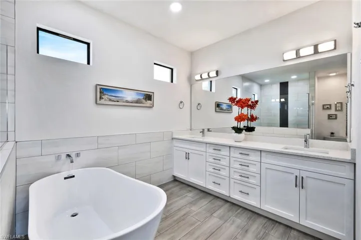 Bathroom with a shower stall, double vanity, a freestanding bath, and tile walls