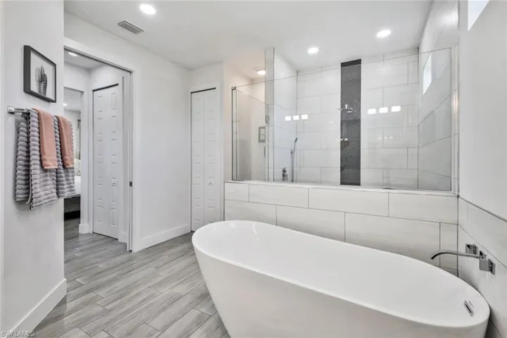 Bathroom with walk in shower, a freestanding bath, a closet, recessed lighting, and wood finished floors
