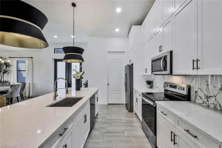 Kitchen with stainless steel appliances, white cabinets, pendant lighting, light stone countertops, and recessed lighting