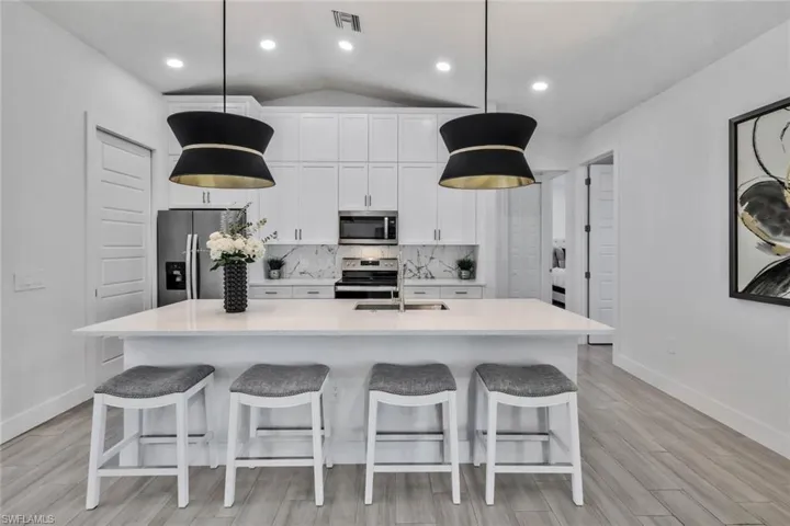 Kitchen with lofted ceiling, white cabinetry, appliances with stainless steel finishes, a kitchen island with sink, and decorative backsplash