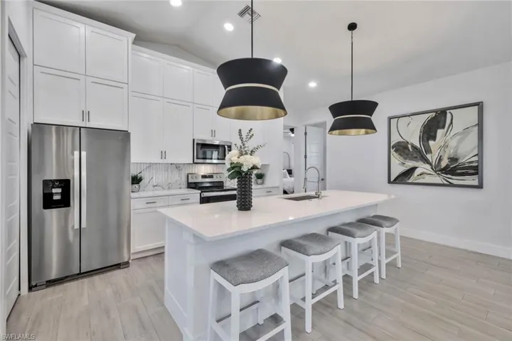 Kitchen with appliances with stainless steel finishes, tasteful backsplash, a breakfast bar area, light wood-style flooring, and lofted ceiling