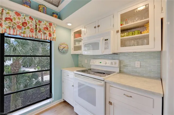 Kitchen featuring white appliances, white cabinets, crown molding, glass fronted cabinets, and backsplash