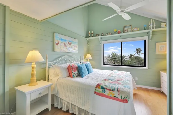 Bedroom with wooden walls, hardwood / wood-style floors, ceiling fan, and lofted ceiling