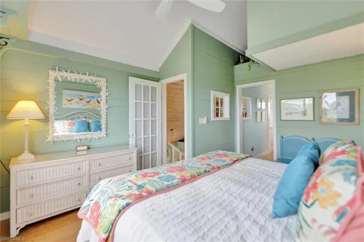 Bedroom with ceiling fan, wooden walls, wood finished floors, and vaulted ceiling