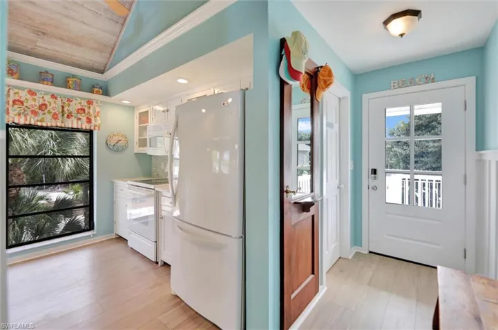 Kitchen with white cabinetry, light countertops, white appliances, light wood-style flooring, and lofted ceiling