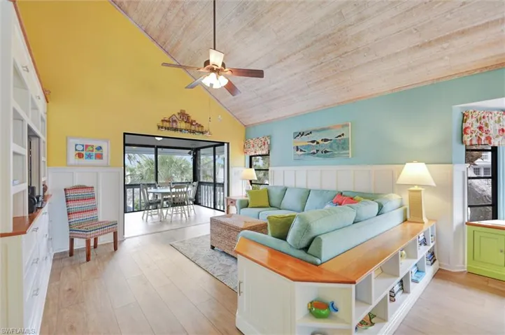 Living room featuring a wainscoted wall, a decorative wall, light wood-style flooring, ceiling fan, and a vaulted wooden ceiling