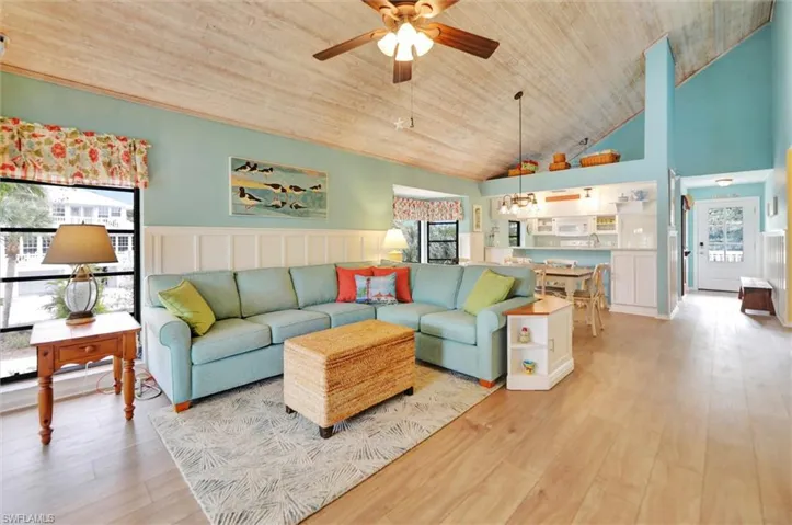 Living room featuring light wood-style flooring, ceiling fan, a decorative wall, a vaulted wooden ceiling, and a wainscoted wall