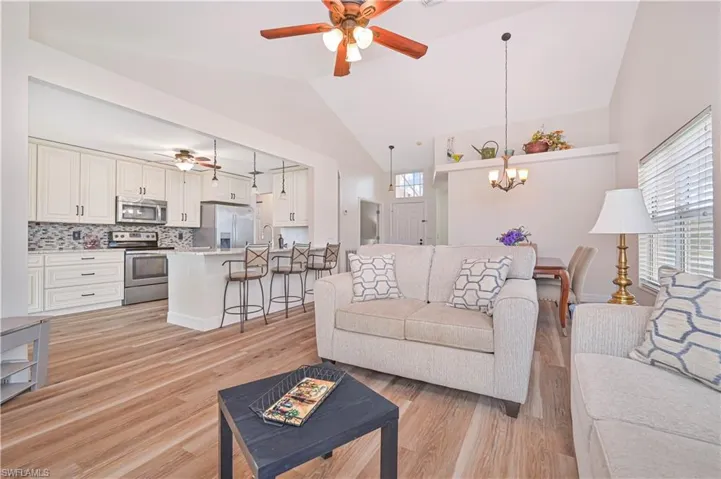 Kitchen featuring cream cabinets, a ceiling fan, dishwasher, light stone countertops, and high vaulted ceiling