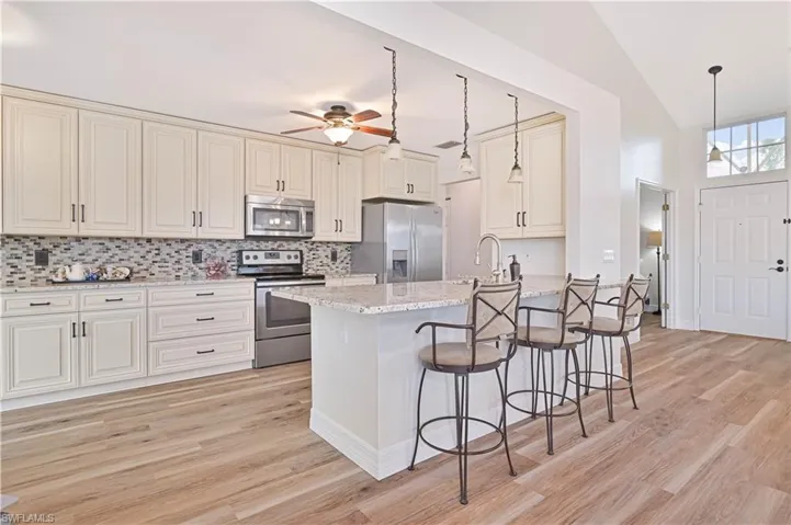 Kitchen with appliances with stainless steel finishes, light stone countertops, cream cabinets, light wood-type flooring, and decorative backsplash