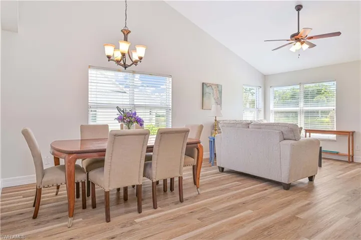 Living room with light wood-style floors, a ceiling fan, vaulted ceiling, and a chandelier