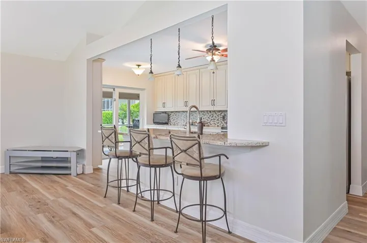 Kitchen with cream cabinets, appliances with stainless steel finishes, decorative light fixtures, and light stone countertops