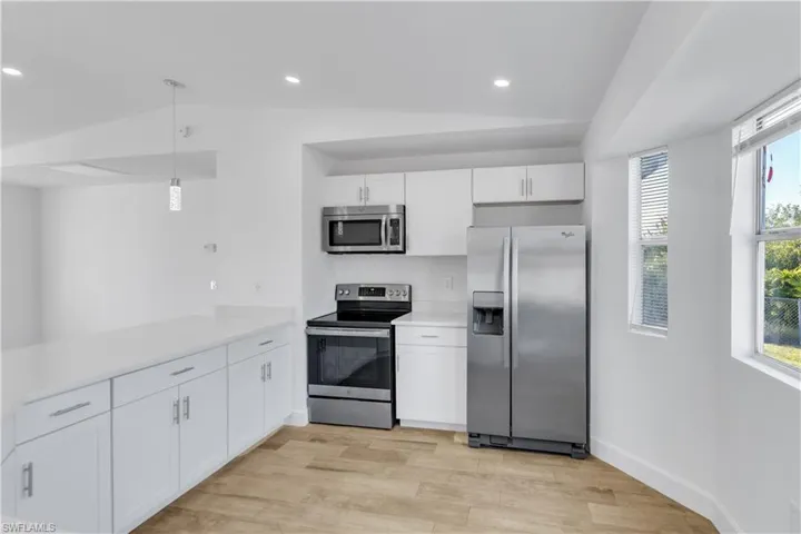 Kitchen featuring light countertops, lofted ceiling, recessed lighting, stainless steel appliances, and white cabinetry