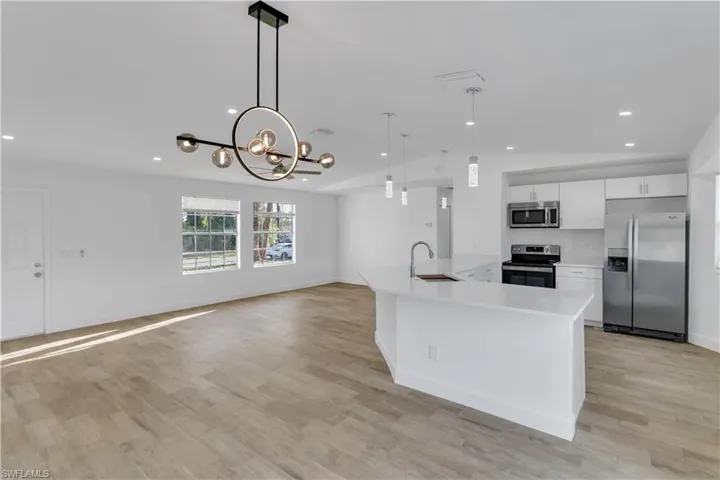 Kitchen with light wood-style flooring, a sink, appliances with stainless steel finishes, white cabinets, and light countertops