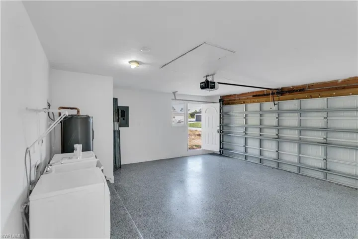 Garage featuring electric panel, separate washer and dryer, a garage door opener, and water heater
