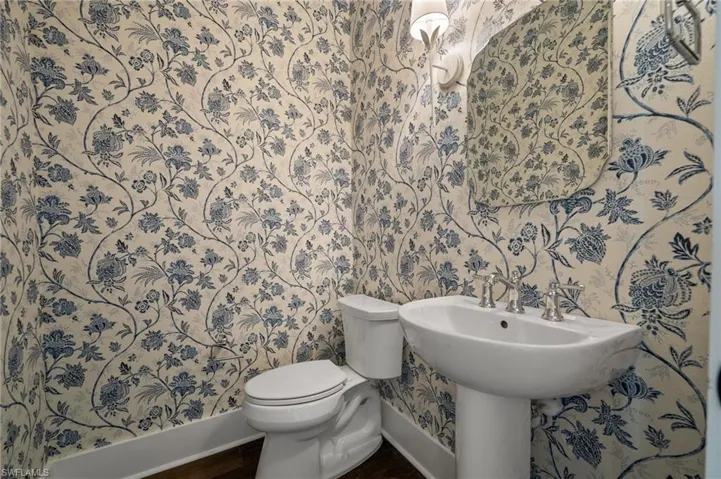 Half bathroom with baseboards, wallpapered walls, toilet, and wood finished floors