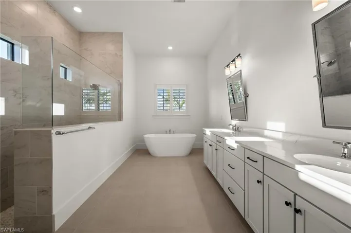 Bathroom with walk in shower, baseboards, a freestanding bath, double vanity, and recessed lighting