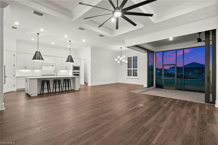 Unfurnished living room with coffered ceiling, a chandelier, a ceiling fan, dark wood finished floors, and ornamental molding