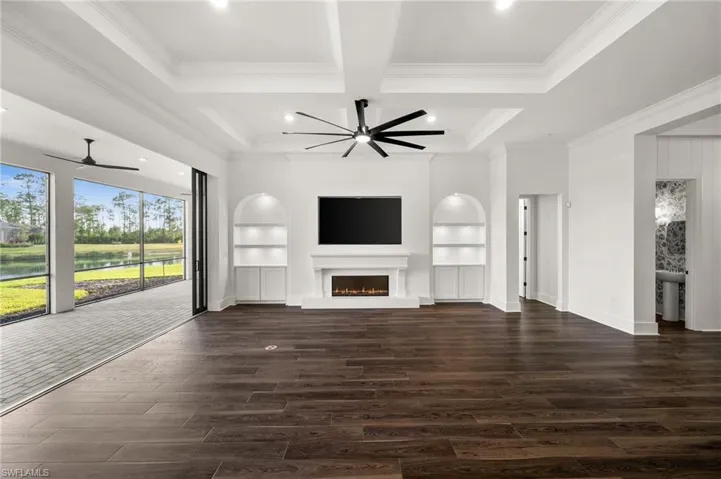 Unfurnished living room featuring a ceiling fan, dark wood-type flooring, coffered ceiling, crown molding, and built in features