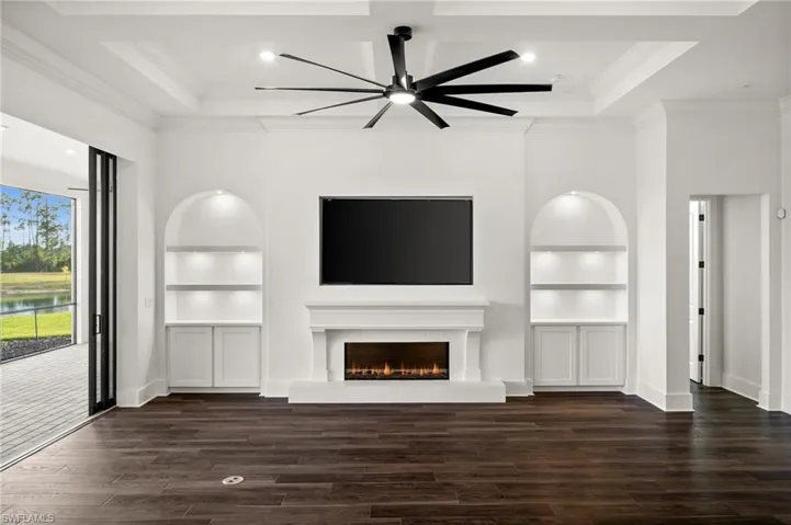 Unfurnished living room with built in features, crown molding, ceiling fan, and wood finished floors