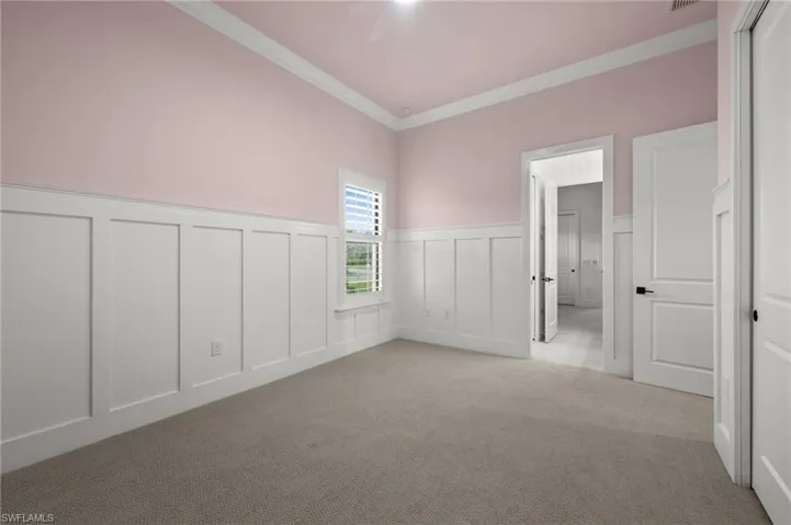Spare room with a decorative wall, light colored carpet, crown molding, and wainscoting