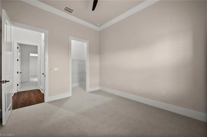 Unfurnished bedroom with carpet, crown molding, baseboards, a walk in closet, and ceiling fan