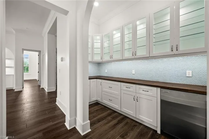 Bar area featuring crown molding, tasteful backsplash, dark wood-style floors, baseboards, and dishwasher