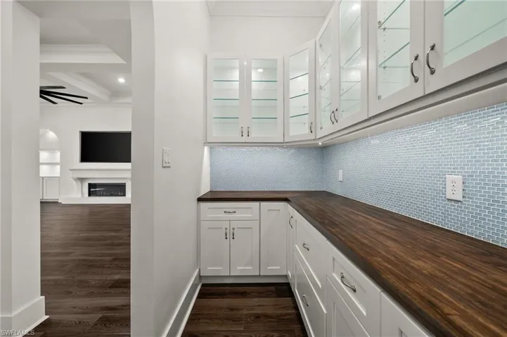 Bar area featuring ornamental molding, backsplash, dark wood-type flooring, a fireplace, and beam ceiling