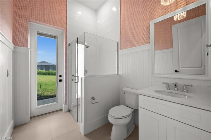 Bathroom with a wainscoted wall, a stall shower, vanity, toilet, and wallpapered walls