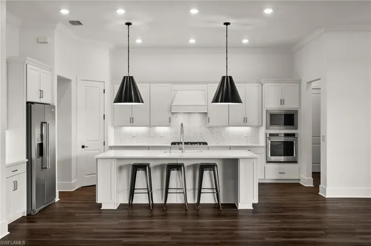 Kitchen featuring appliances with stainless steel finishes, custom range hood, light countertops, an island with sink, and crown molding