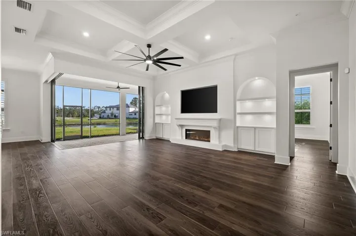 Unfurnished living room featuring ceiling fan, dark wood-type flooring, a glass covered fireplace, baseboards, and ornamental molding