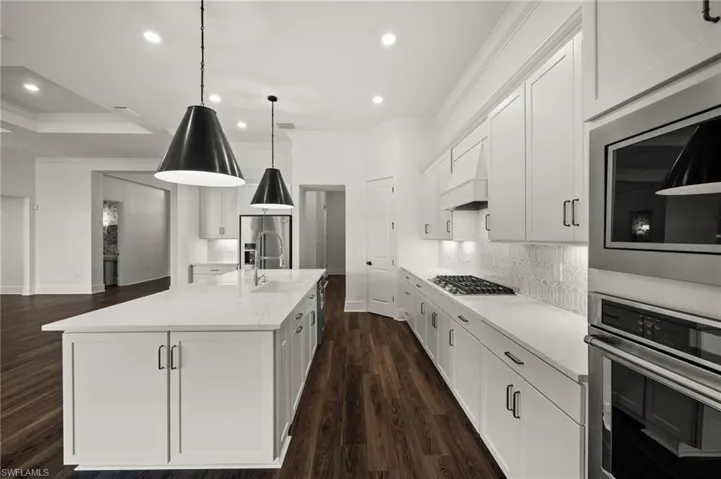 Kitchen with stainless steel appliances, ornamental molding, white cabinetry, a sink, and recessed lighting
