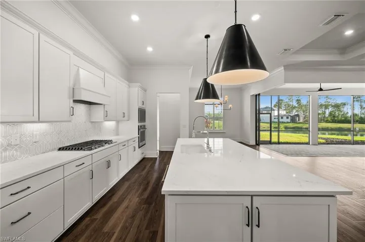 Kitchen featuring a sink, custom exhaust hood, appliances with stainless steel finishes, crown molding, and a kitchen island with sink