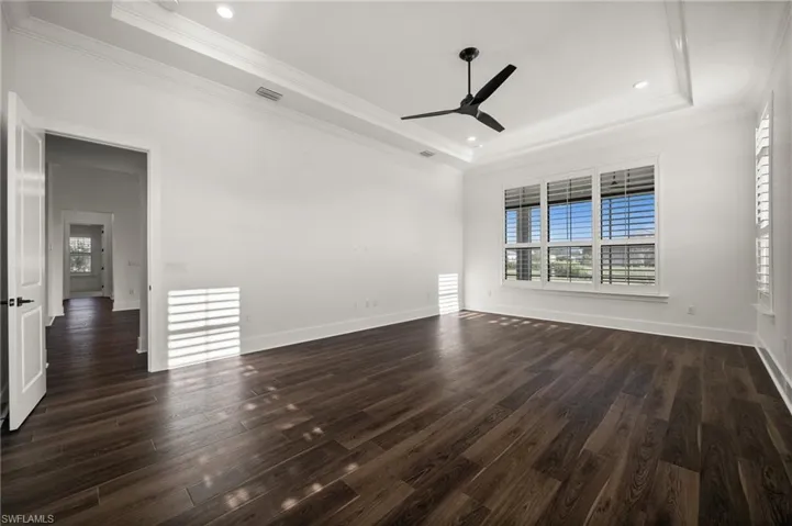 Spare room with a tray ceiling, ceiling fan, dark wood-type flooring, crown molding, and baseboards