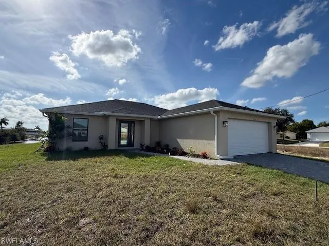 Ranch-style home with an attached garage, stucco siding, a front lawn, and decorative driveway