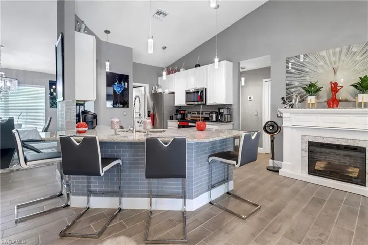 Kitchen with light wood Tile flooring, white cabinetry, hanging light fixtures, a kitchen breakfast bar, and appliances with stainless steel finishes