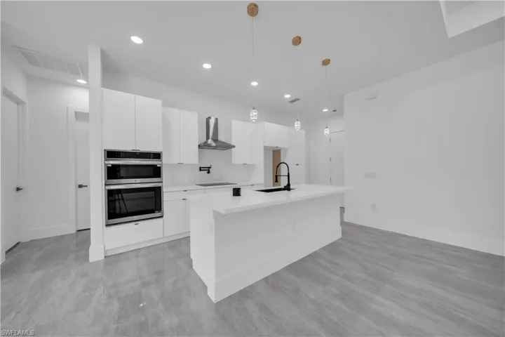Kitchen with white cabinetry, hanging light fixtures, recessed lighting, wall chimney range hood, and stainless steel double oven