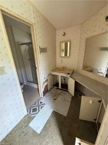 Full bath with a textured ceiling, a shower stall, and wallpapered walls