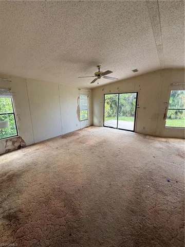 Spare room with carpet floors, a textured ceiling, vaulted ceiling, and ceiling fan