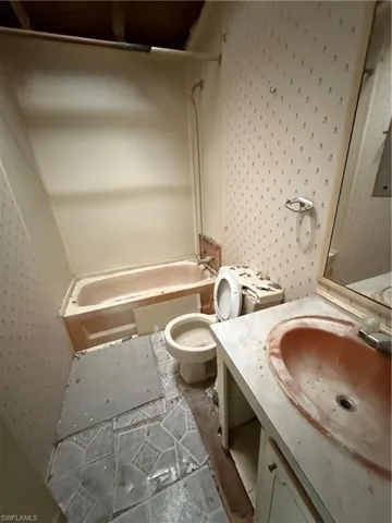 Bathroom with shower / tub combination, vanity, and wallpapered walls