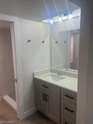Full bathroom featuring vanity, baseboards, a tile shower, and wood finished floors