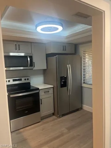 Kitchen featuring fridge with ice dispenser, ornamental molding, gray cabinets, a tray ceiling, and stove