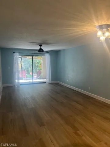Spare room featuring baseboards, ceiling fan with notable chandelier, and wood finished floors