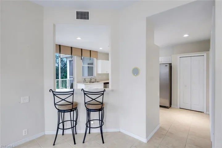 Kitchen featuring a kitchen bar, white cabinetry, light countertops, stainless steel refrigerator, and recessed lighting