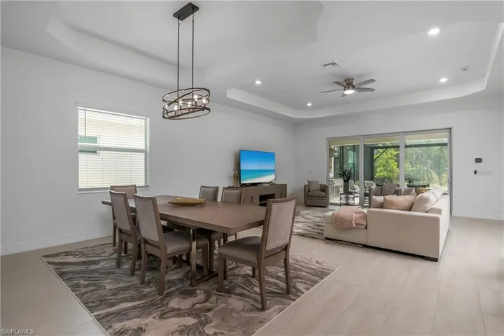 Dining area with a raised ceiling, recessed lighting, a ceiling fan, and a chandelier