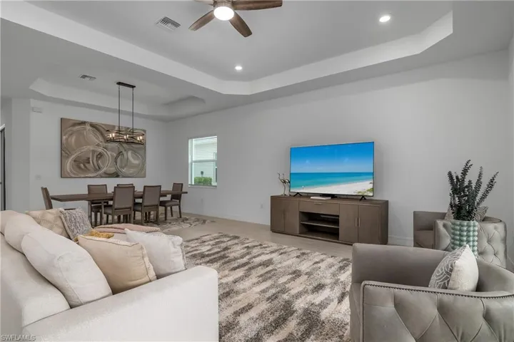 Living room with a raised ceiling, a ceiling fan, a chandelier, and recessed lighting
