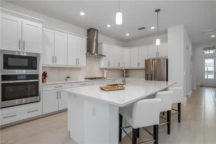 Kitchen featuring appliances with stainless steel finishes, wall chimney exhaust hood, a kitchen breakfast bar, light countertops, and pendant lighting