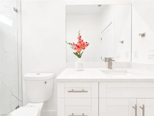 Bathroom featuring a white vanity with brushed nickel hardware, an integrated sink, and a speckled white countertop