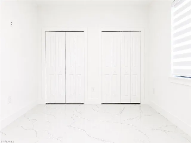 Bright interior space featuring two white bi-fold closet doors, lustrous marble-look floor tiling, and a window with horizontal blinds