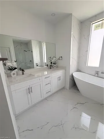 Full bathroom with a marble finish shower, a soaking tub, light marble finish flooring, and double vanity